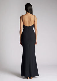Back iimage of a model wearing a black maxi dress with a v-neckline, thin straps with twist front detail at bust, low back and subtle flair at hem. The design featured is the Vesper Marlowe Black Maxi Dress
