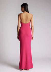 Back image of a model wearing a cerise pink maxi dress, featuring a v-neckline, thin straps with twist front detail at bust, low back and subtle flair at hem. The style featured is Vesper Marlowe Cerise Maxi Dress.