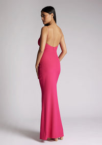 Quarter back image of a model wearing a cerise pink maxi dress, featuring a v-neckline, thin straps with twist front detail at bust, low back and subtle flair at hem. The style featured is Vesper Marlowe Cerise Maxi Dress.