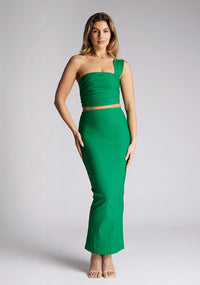 Front image of a blonde model wearing a emerald one shoulder top with a one-shoulder cut and straight neckline, side pleating and a size zip. The design featured is the Vesper Matilda Emerald One Shoulder Top pair with Vesper Hana Emerald Skirt