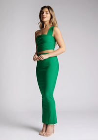 Front  quarter image of a blonde model wearing a emerald one shoulder top with a one-shoulder cut and straight neckline, side pleating and a size zip. The design featured is the Vesper Matilda Emerald One Shoulder Top pair with Vesper Hana Emerald Skirt