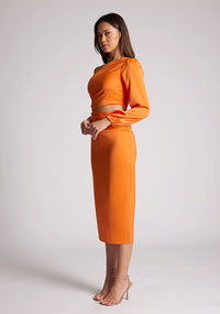 Quarter front image of a model wearing an orange midi  dress, featuring an asymmetric neckline with one sleeve, with a side waist cut-out detail.The dress featured is the Vesper Niccola Orange Midi Dress.