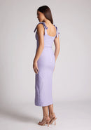 Back quarter image of a model wearing a lilac midaxi dress with a featuring scoop neckline, tie shoulder straps up, front skirt split and bodycon fit accentuates curves for finesse. The design featured is the Vesper Onyx Lilac Midaxi Dress