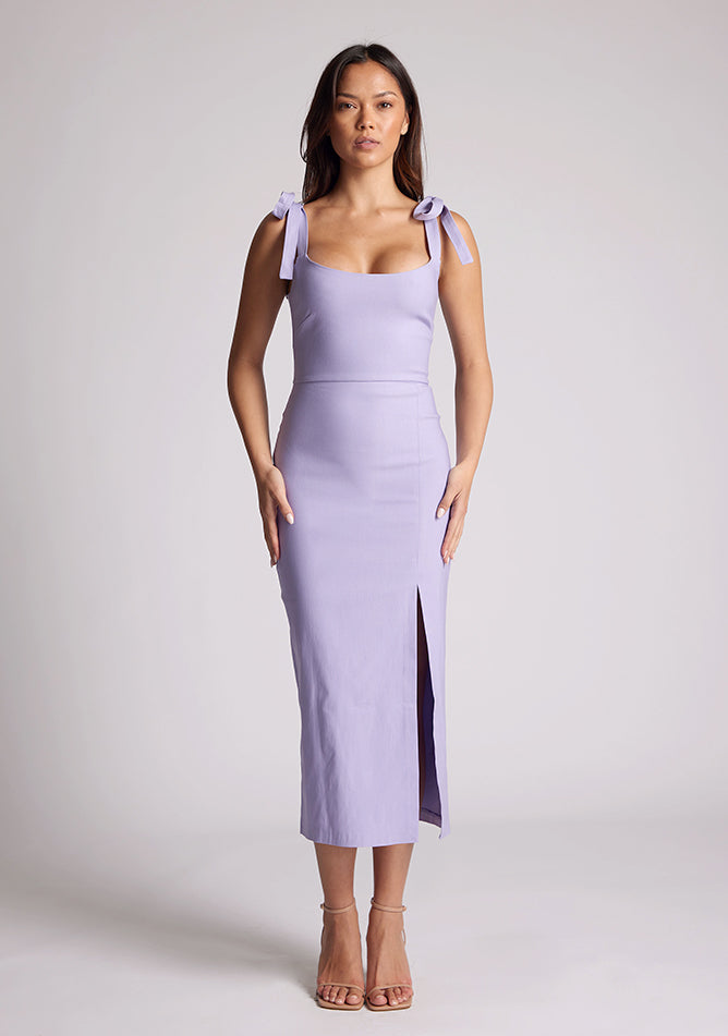Front image of a model wearing a lilac midaxi dress, featuring tie up straps and a front skirt split. The dress featured is the Vesper Onyx lilac midaxi dress
