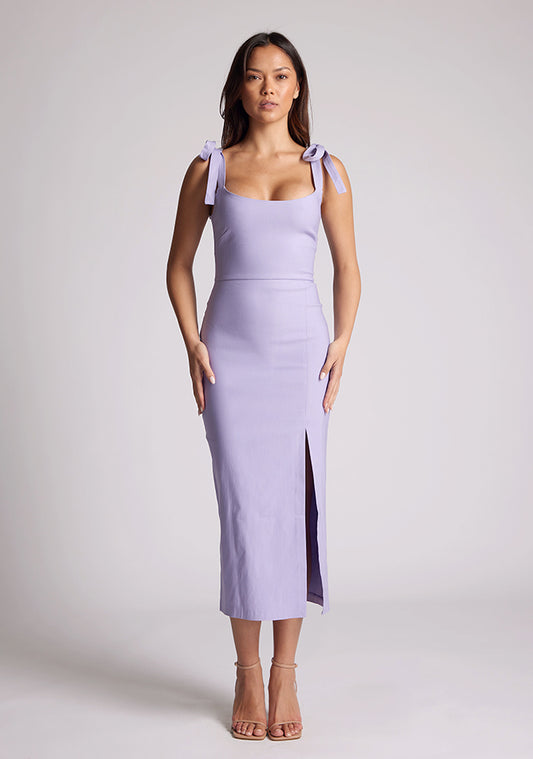 Front image of a model wearing a lilac midaxi dress with a featuring scoop neckline, tie shoulder straps up, front skirt split and bodycon fit accentuates curves for finesse. The design featured is the Vesper Onyx Lilac Midaxi Dress