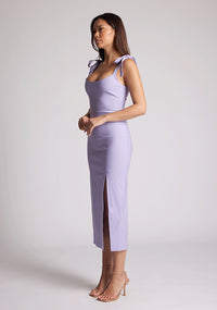 Front quarter image of a model wearing a lilac midaxi dress with a featuring scoop neckline, tie shoulder straps up, front skirt split and bodycon fit accentuates curves for finesse. The design featured is the Vesper Onyx Lilac Midaxi Dress