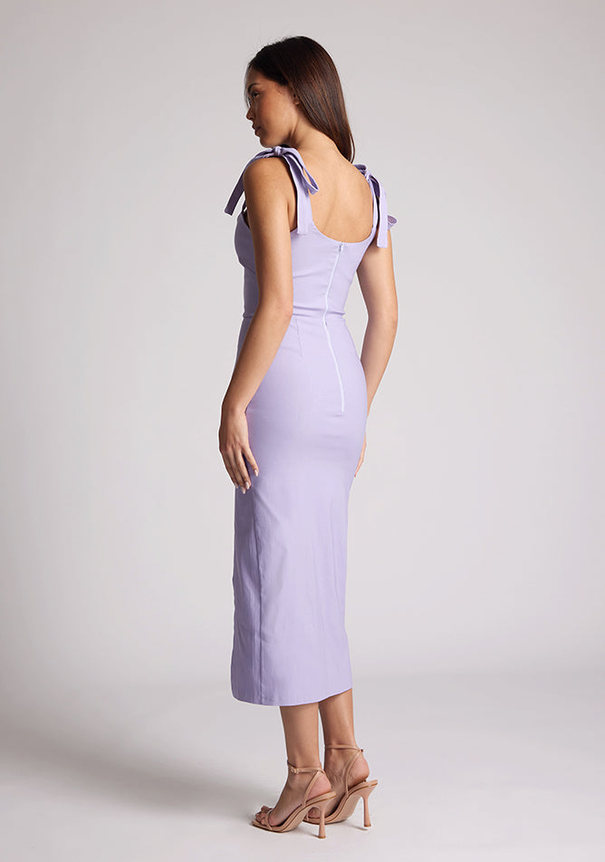 Quarter back  image of a model wearing a lilac midaxi dress, featuring tie up straps and a front skirt split. The dress featured is the Vesper Onyx lilac midaxi dress