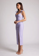 Quarter front image of a model wearing a lilac midaxi dress, featuring tie up straps and a front skirt split. The dress featured is the Vesper Onyx lilac midaxi dress