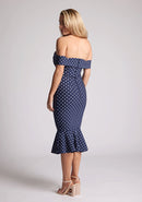 Back quarter image of the model wearing a navy polka bardot midaxi dress with a classy bardot neckline with arm bands and frill hem detail. The design featured is the Vesper Racquel Navy Polka Dot Bardot Midaxi Dress
