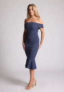 Front quarter image of the model wearing a navy polka bardot midaxi dress with a classy bardot neckline with arm bands and frill hem detail. The design featured is the Vesper Racquel Navy Polka Dot Bardot Midaxi Dress