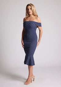 Front quarter image of the model wearing a navy polka bardot midaxi dress with a classy bardot neckline with arm bands and frill hem detail. The design featured is the Vesper Racquel Navy Polka Dot Bardot Midaxi Dress