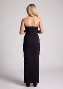 Back image of a model wearing a black maxi dress with a straight strapless neckline, body-hugging silhouette, front skirt split and invisible centre back zip. The design featured is the Vesper Raine Black Strapless Maxi Dress