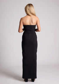 Back image of a model wearing a black maxi dress with a straight strapless neckline, body-hugging silhouette, front skirt split and invisible centre back zip. The design featured is the Vesper Raine Black Strapless Maxi Dress