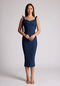 Front image of a model wearing a navy midaxi dress, featuring a self-tie strappy bows, pleated cup details at bust, bodycon fit with statement gold zip at centre back .The dress featured is the Vesper Rapunzel Navy Midaxi Dress