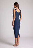 Quarter back image of a model wearing a navy midaxi dress, featuring a self-tie strappy bows, pleated cup details at bust, bodycon fit with statement gold zip at centre back .The dress featured is the Vesper Rapunzel Navy Midaxi Dress