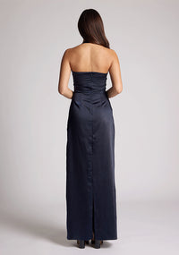 Back image of a model wearing a navy Maxi Dress with a halter cowl neck exudes sophistication, while the lustrous satin fabric offers a luxurious touch, the design features the Vesper Saige Navy Maxi Dress