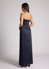 Quarter back image of a model wearing a navy Maxi Dress with a halter cowl neck exudes sophistication, while the lustrous satin fabric offers a luxurious touch, the design features the Vesper Saige Navy Maxi Dress