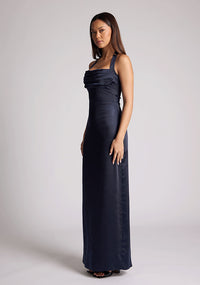 Quarter front image of a model wearing a navy Maxi Dress with a halter cowl neck exudes sophistication, while the lustrous satin fabric offers a luxurious touch, the design features the Vesper Saige Navy Maxi Dress