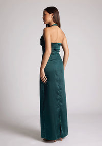 Back quarter image of a  model wearing a pine maxi dress with a halter cowl neck exudes sophistication, while the lustrous satin fabric offers a luxurious touch. The design featured is the Vesper Saige Pine Satin Green Maxi Dress