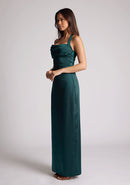 Front quarter image of a  model wearing a pine maxi dress with a halter cowl neck exudes sophistication, while the lustrous satin fabric offers a luxurious touch. The design featured is the Vesper Saige Pine Satin Green Maxi Dress