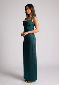 Front quarter image of a  model wearing a pine maxi dress with a halter cowl neck exudes sophistication, while the lustrous satin fabric offers a luxurious touch. The design featured is the Vesper Saige Pine Satin Green Maxi Dress