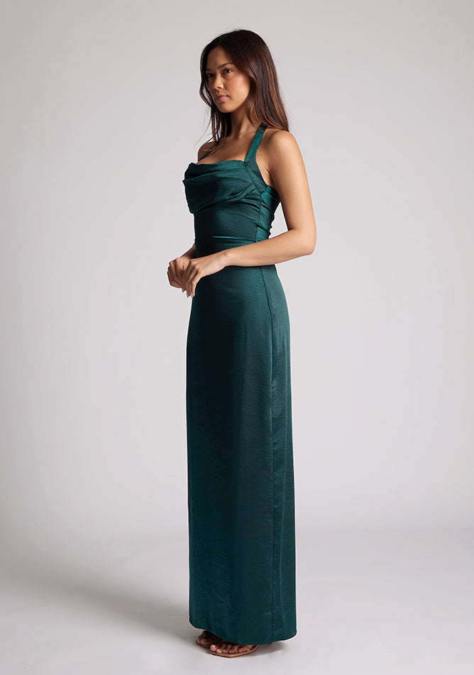Front quarter image of a  model wearing a pine maxi dress with a halter cowl neck exudes sophistication, while the lustrous satin fabric offers a luxurious touch. The design featured is the Vesper Saige Pine Satin Green Maxi Dress