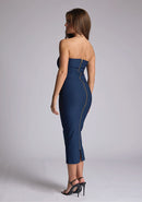 Back quarter image of a model wearing a navy midaxi dress, featuring a strapless neckline with gold zip at the back. The design featured is the Vesper Shelbie Navy Strapless Midaxi Dress