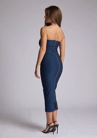 Back quarter image of a model wearing a navy midaxi dress, featuring a strapless neckline with gold zip at the back. The design featured is the Vesper Shelbie Navy Strapless Midaxi Dress