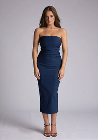 Front image of a model wearing a navy midaxi dress, featuring a strapless neckline with gold zip at the back. The design featured is the Vesper Shelbie Navy Strapless Midaxi Dress