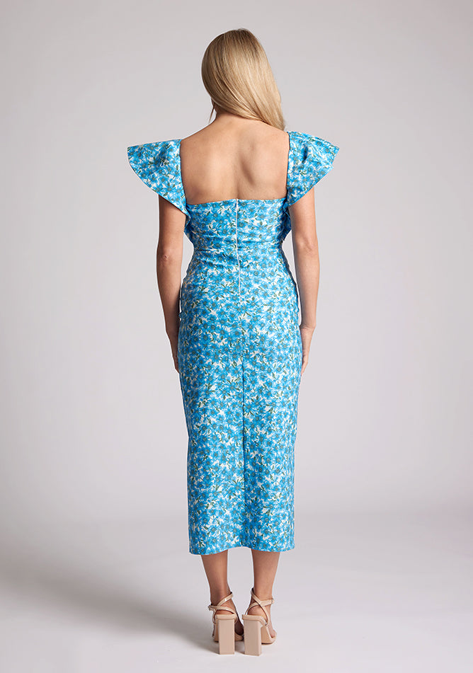 Back image of blonde model wearing a blue floral short sleeve midaxi dress with a sweetheart neckline, short frill hem cap sleeves and a front skirt split. The design featured is Vesper Sunday Blue Floral Short Sleeve Midaxi Dress