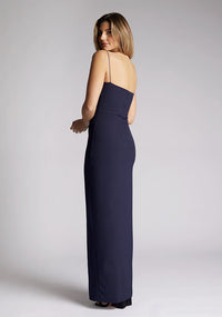 Back quarter image of a model wearing a navy maxi dress, featuring delicate straps and a front skirt split. The design featured is the Vesper Tate Navy Maxi Dress