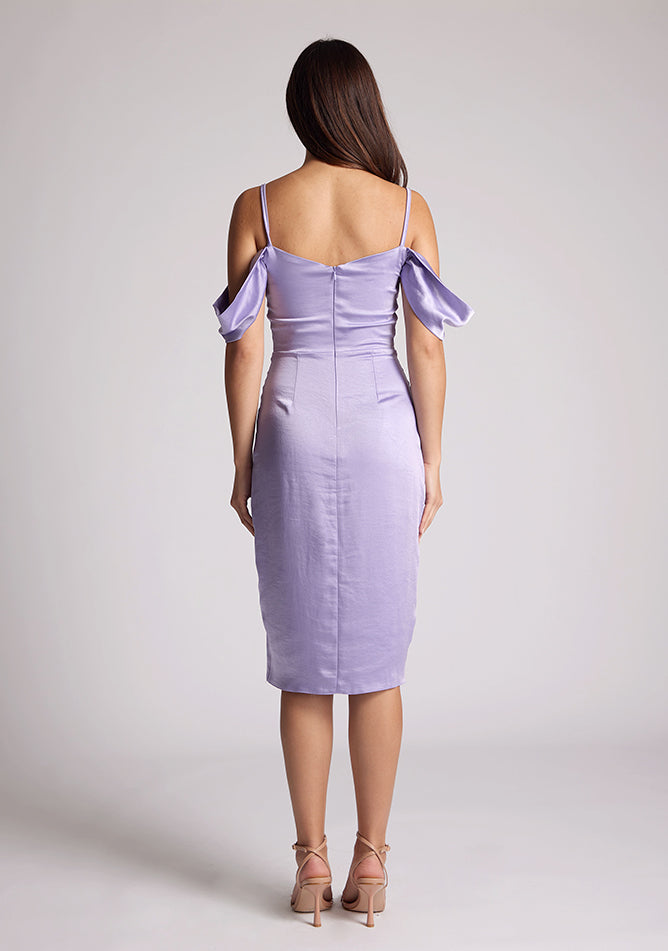 Back image of a brunette model wearing a lilac midi dress, featuring a subtle cowl neckline, thin straps and draped arm bands and an invisible centre back zip. The dress featured is the Vesper Victoria Lilac Satin Bardot Midi Dress