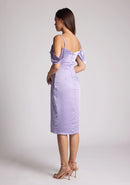 Quarter Back image of a brunette model wearing a lilac midi dress, featuring a subtle cowl neckline, thin straps and draped arm bands and an invisible centre back zip. The dress featured is the Vesper Victoria Lilac Satin Bardot Midi Dress
