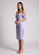 Quarter front image of a brunette model wearing a lilac midi dress, featuring a subtle cowl neckline, thin straps and draped arm bands and an invisible centre back zip. The dress featured is the Vesper Victoria Lilac Satin Bardot Midi Dress
