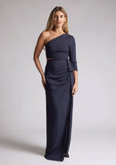 Front image of a blonde model wearing a  Navy Maxi Dress with an asymmetric long-sleeve design, coupled with a tasteful front cutout, creates a uniquely stylish statement. The design features is the Vesper Vienna Navy One Sleeve Maxi Dress