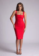 Front image of model wearing a red pencil dress with a square-cut neckline and straps and a bodycon fit. The design features is the Vesper Zada Red Bodycon Pencil Midi Dress