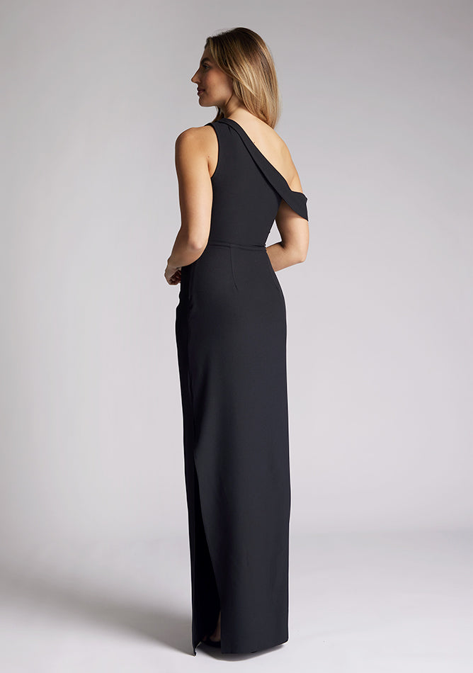 Back quarter  image of a model wearing a black maxi dress, featuring a one shoulder design with a band that encompasses the opposite arm. The dress featured is the Vesper Yvette black maxi dress