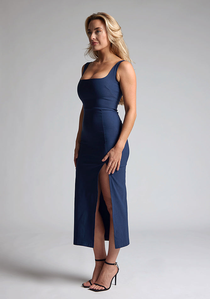 Quarter side image of the model wearing a Navy Bodycon Midaxi Dress with a square neckline with wide straps, and a front skirt split, a design features Vesper Abbie Navy Bodycon Midaxi Dress