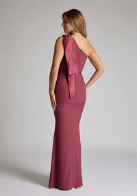 Quarter back of blonde model wearing an Burgundy Maxi Dress with a asymmetric design, chic one-shoulder detail, dress featured is Vesper Deven Burgundy Maxi Dress