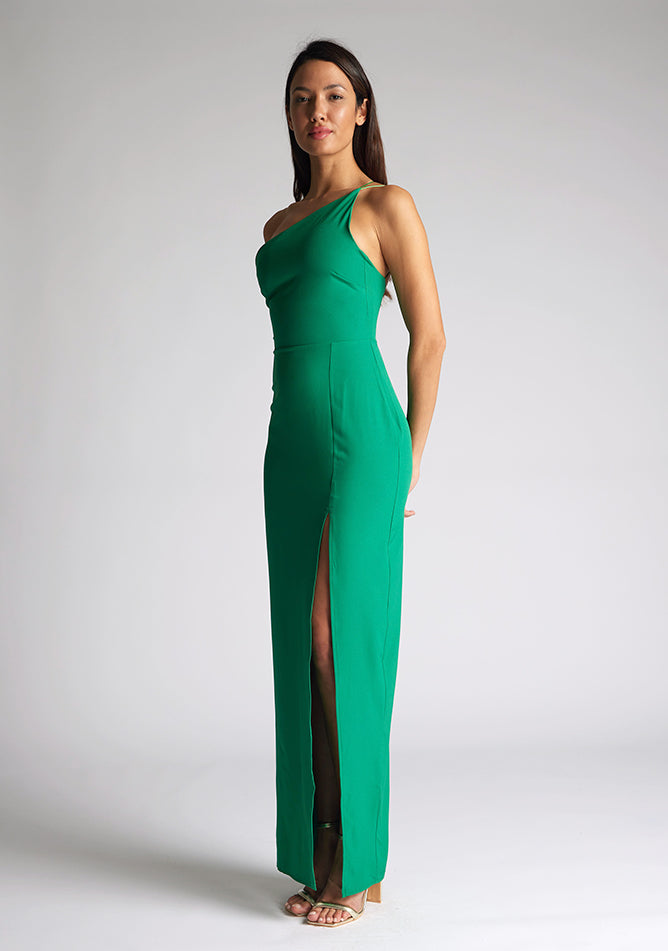 Quarter front image of a model wearing an emerald green maxi dress with an asymmetric neckline, one shoulder strap, front skirt split and open back with asymmetric strap detail across back. The style featured is the Vesper Florian Emerald Green Maxi Dress