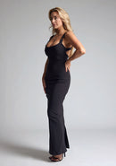 Front quarter image of a model wearing a black maxi dress, featuring metal detailing on the straps and a back strap detail. The dress featured is the Vesper Jessica black maxi dress