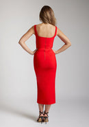 Back image of a blonde model wearing a red bodycon midaxi dress with a square neckline with wide straps and a front skirt split. The design featured is the Vesper Abbie Red Bodycon Midaxi Dress