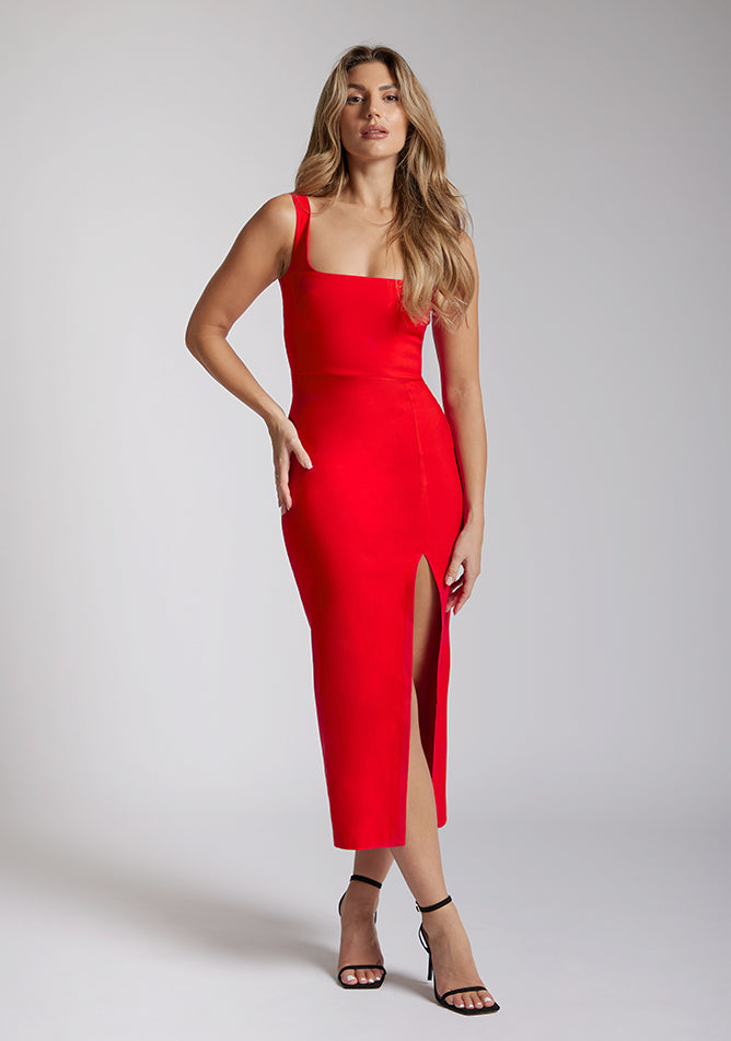 Front image of blonde model wearing a red bodycon midaxi dress with a square neckline with wide straps and a front skirt split. The design featured is the Vesper Abbie Red Bodycon Midaxi Dress