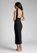 Back quarter image of a model wearing a black cross neck midaxi dress with a crossover neck detail with flattering open back and a high leg split. The design featured is the Vesper Aida Black Cross Neck Midaxi Dress