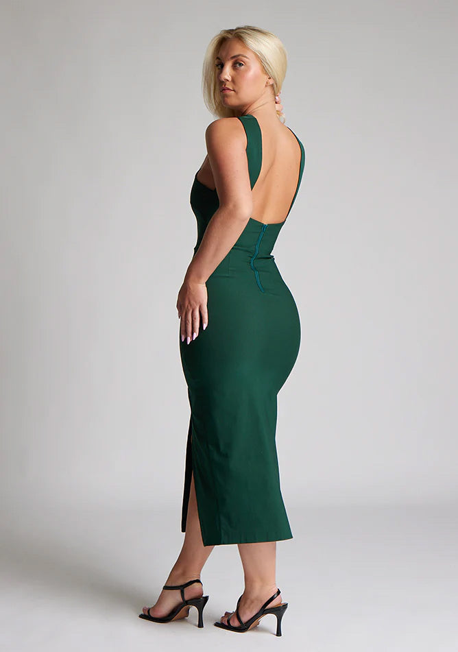 Back quarter image of blonde model wearing a forest green midaxi dress with a  flattering open back and ultra-sexy high leg split and a crossover neckline design. The design featured is the Vesper Aida Forest Green Cross Neck Midaxi Dress