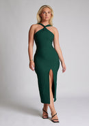 Front image of blonde model wearing a forest green midaxi dress with a  flattering open back and ultra-sexy high leg split and a crossover neckline design. The design featured is the Vesper Aida Forest Green Cross Neck Midaxi Dress