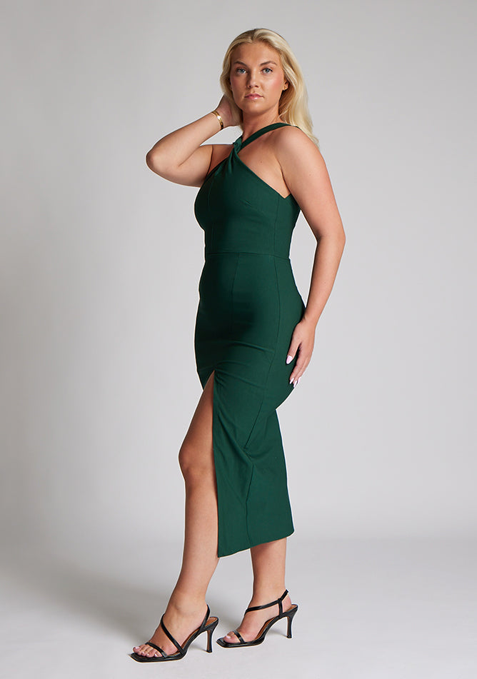 Front quarter image of blonde model wearing a forest green midaxi dress with a  flattering open back and ultra-sexy high leg split and a crossover neckline design. The design featured is the Vesper Aida Forest Green Cross Neck Midaxi Dress
