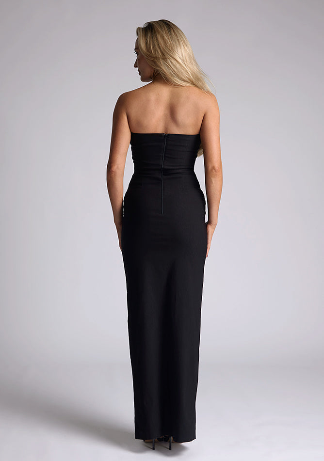 Back image of a model wearing a black strapless maxi dress with a front split and centre back zip. The design featured is the Vesper Vesper Alaya Black Maxi Dress
