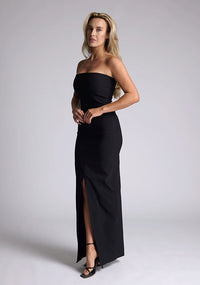 Front quarter image of a model wearing a black strapless maxi dress with a front split and centre back zip. The design featured is the Vesper Alaya Black Maxi Dress