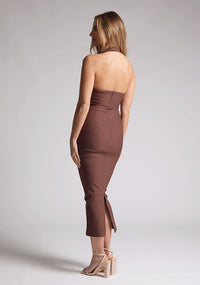 Back quarter image of a blonde model wearing a chocolate midaxi dress with a halter neckline, sleeveless, and a back skirt split. The design features is the Vesper Asher Chocolate Halter Neck Midaxi Dress